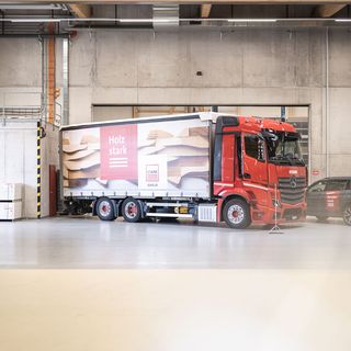 Rot lackierter Stark AG Lastwagen in Lagerhalle, mit Holzwerkstoff-Werbung aufgeladen.