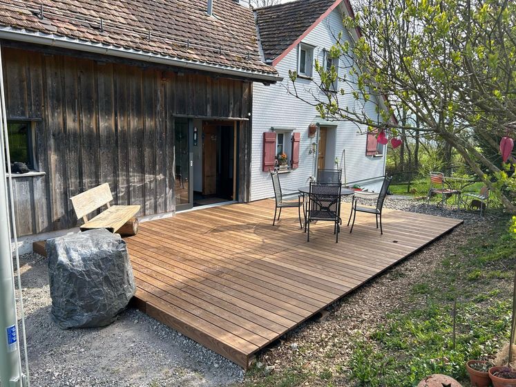 Holzterrasse mit Sitzgelegenheiten vor einem Haus im Garten.