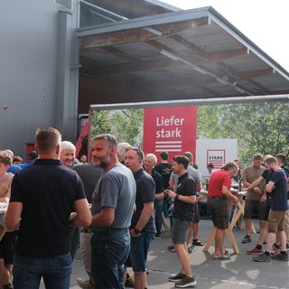 Mitarbeiter der Stark AG in entspannter Atmosphäre bei einem Firmenevent im Freien vor einem Lieferfahrzeug.