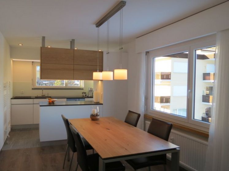 Moderne Küche mit Holztisch und Hängelampen in einem lichtdurchfluteten Raum.