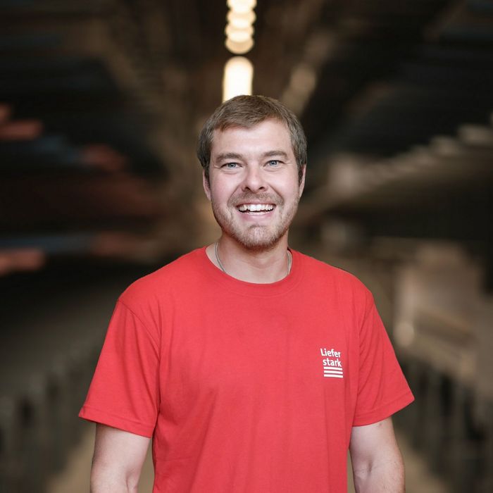 Stark Teammitglied Lächelt Lächelnder Mann in rotem T-Shirt mit Stark-Logo in einem Lagerraum.