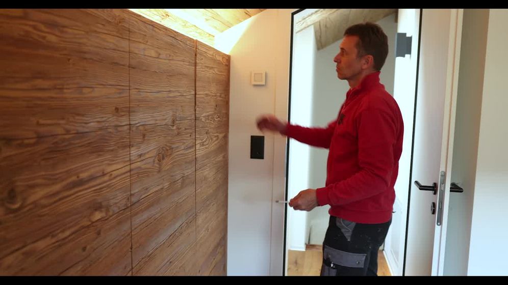 Ein Mann arbeitet an einer Wand mit hölzernen Akustikpaneelen in einem modernen Innenraum.