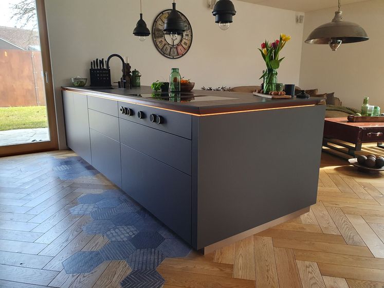 Moderne Küche mit stilvollem Holzboden und dunkler Kücheninsel bei Tageslicht.