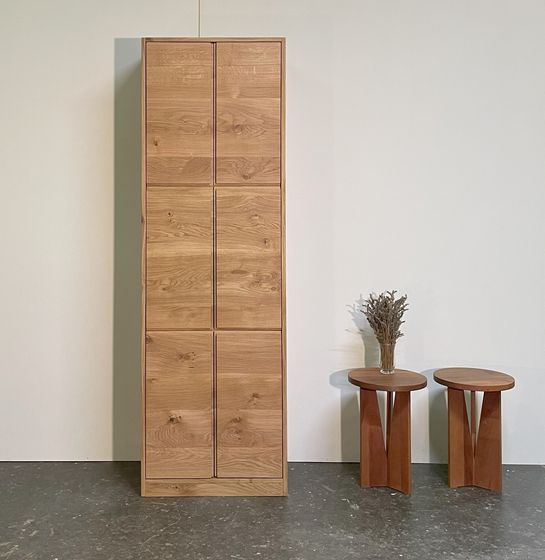 Holzschrank und Holztische mit Vase vor weisser Wand.