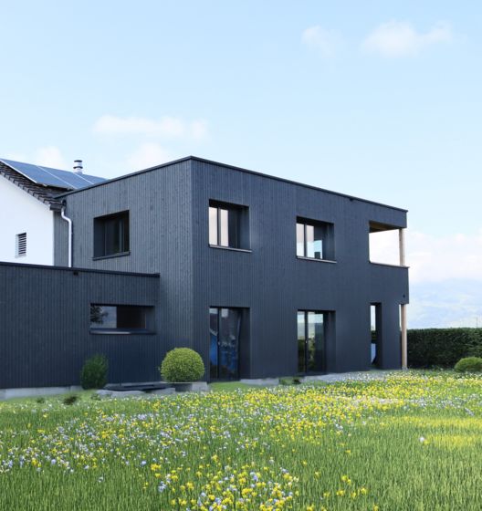 Modernes Holzhaus mit blühender Wiese im Vordergrund.