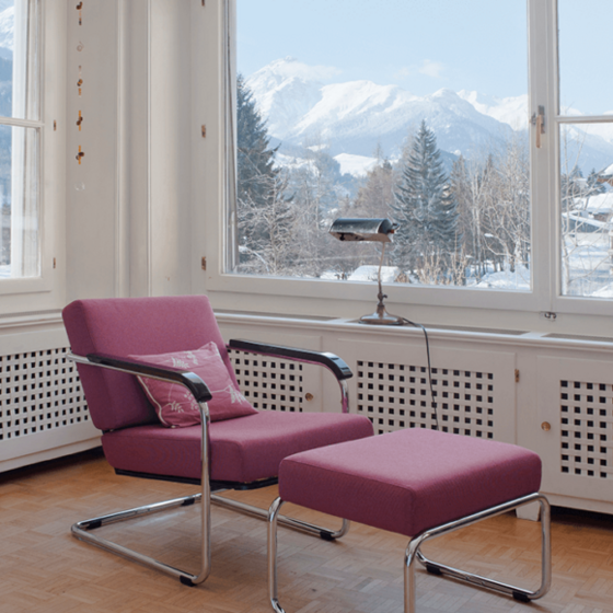 Modernes Wohnzimmer mit lila Sessel und Blick auf schneebedeckte Berge.