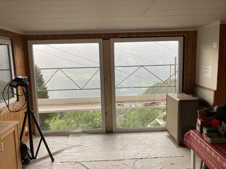 Innenraum mit grosser Fensterfront und Bergblick, umgeben von Gerüsten.