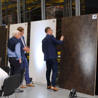 Drei Männer betrachten grosse Holzplatten in einem Lagerraum der Stark AG.