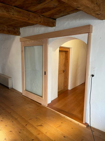 Holz-Schiebetür in modernem Innenraum mit Holzboden und Holzbalkendecke.