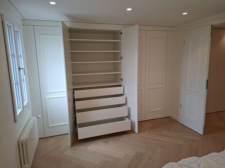 Moderner Einbauschrank mit geöffneter Tür und Schubladen in einem hellen Raum mit Holzfussboden.