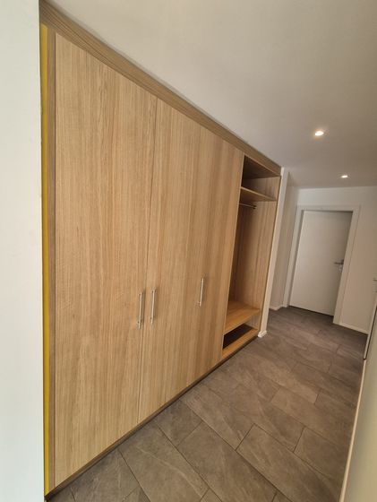 Ein moderner Einbauschrank aus hellem Holz in einem Flur mit grauen Fliesen.