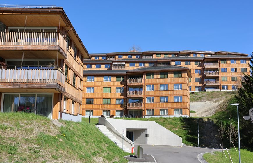 Mehrstöckiges Wohngebäude mit Holzfassade vor blauem Himmel.
