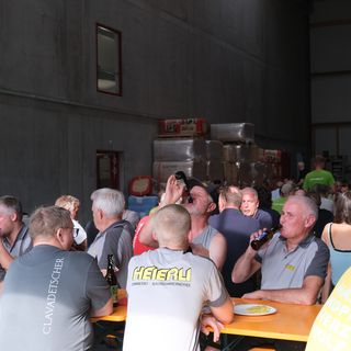 Mitarbeiter bei einer Veranstaltung in einer Lagerhalle an Biertischen sitzend.