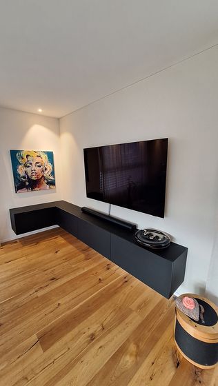 Modernes Wohnzimmer mit Holzboden, schwarzem TV-Möbel und Kunstbild an der Wand.