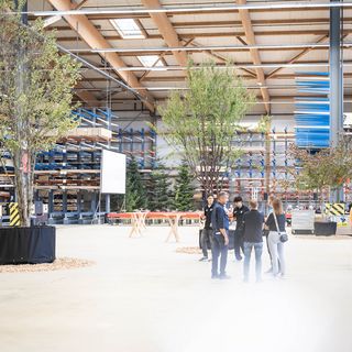 Menschen in einer modernen Lagerhalle mit Holzprodukten bei einer Veranstaltung.