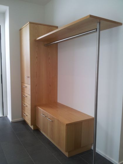 Moderner Holzschrank mit Sitzbank und Kleiderstange in hellem Raum.