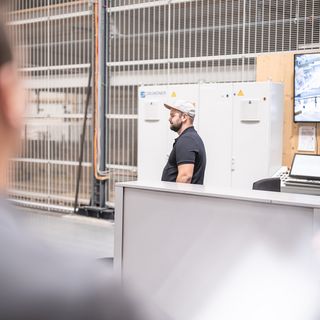 Mitarbeiter in Lagerhalle mit Überwachungsbildschirmen im Hintergrund.