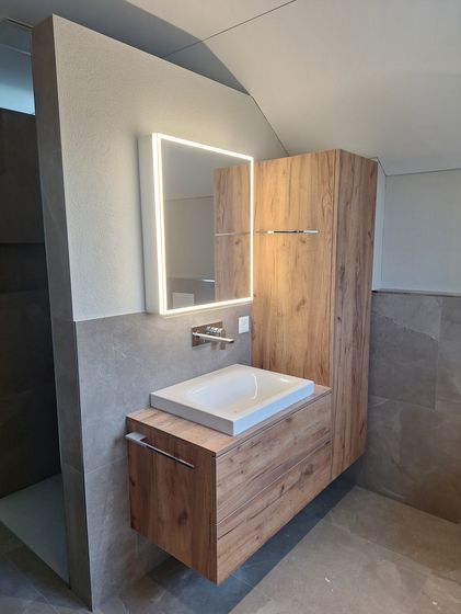 Modernes Badezimmer mit hölzernem Waschtisch und beleuchtetem Spiegel.
