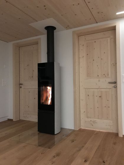 Moderner Holzofen zwischen Holztüren in einem Raum mit Holzboden und Holzdecke.
