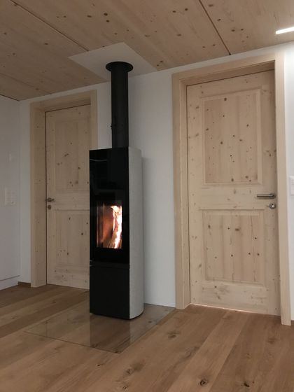 Moderner Holzofen zwischen Holztüren in einem Raum mit Holzboden und Holzdecke.