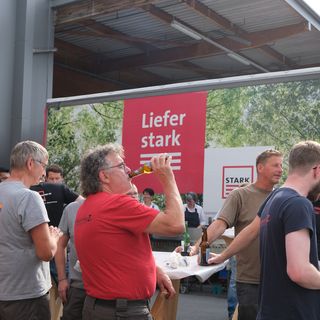 Mitarbeiter der Stark AG feiern gemeinsam vor einem Banner mit der Aufschrift 'Liefer stark' bei einem informellen Treffen.