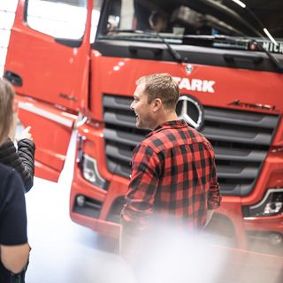 Personen unterhalten sich vor einem roten Stark-LKW in einer Halle.