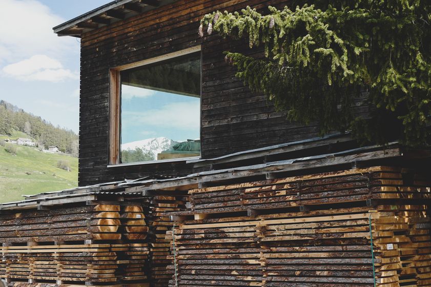Gestapelte Holzstapel vor einem Holzhaus in alpiner Landschaft.