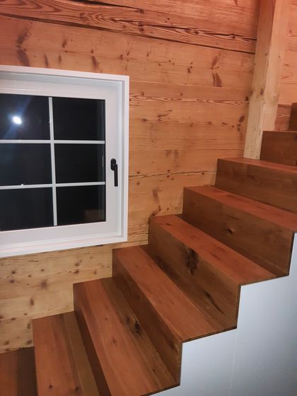 Holztreppe neben einem weissen Fenster in einem Innenraum mit Holzverkleidung.
