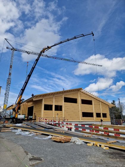 Holzgebäude im Bau mit Kran vor blauem Himmel.
