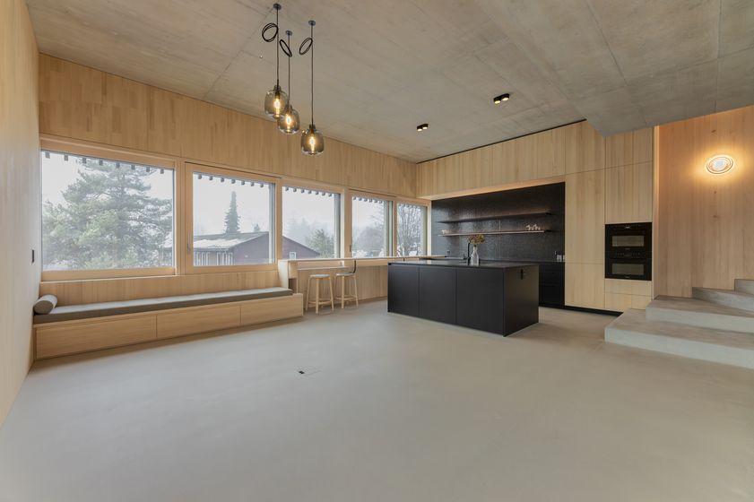 Moderne Küche mit Holzverkleidung und grossen Fenstern, die einen Ausblick auf Bäume bieten.