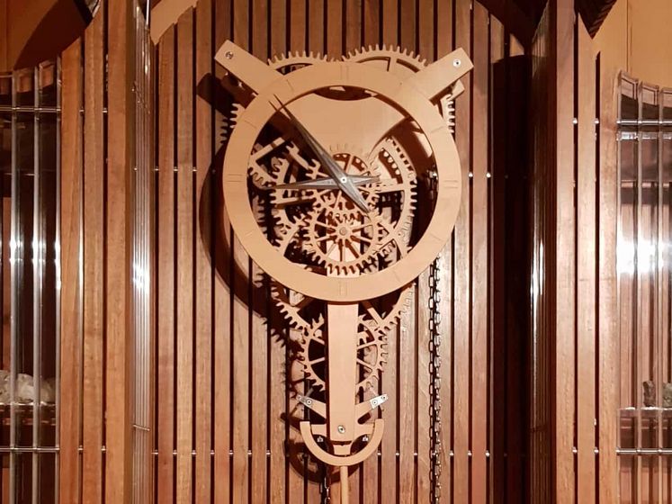 Holzuhr mit sichtbarem Zahnradmechanismus vor Holzverkleidung.