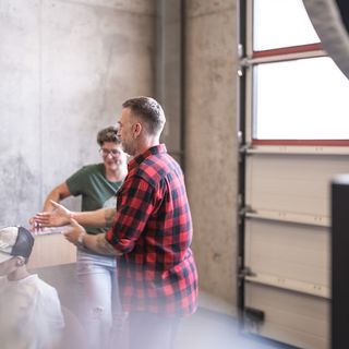 Eine Gruppe von Menschen unterhält sich in einem industriellen Raum mit Betonwänden.