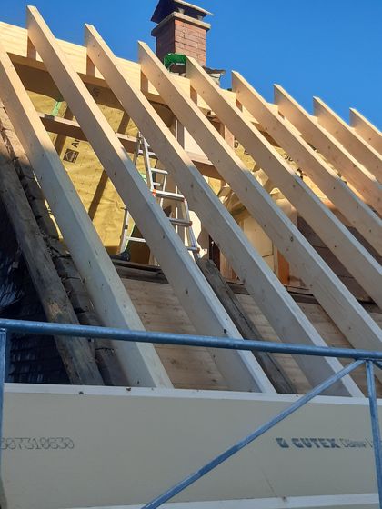 Dachkonstruktion mit Holzträgern auf einer Baustelle unter klarem Himmel.