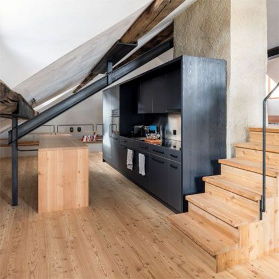 Moderne Küche mit Holz- und Akzentelementen in einem offenen Raum mit schrägem Dach.