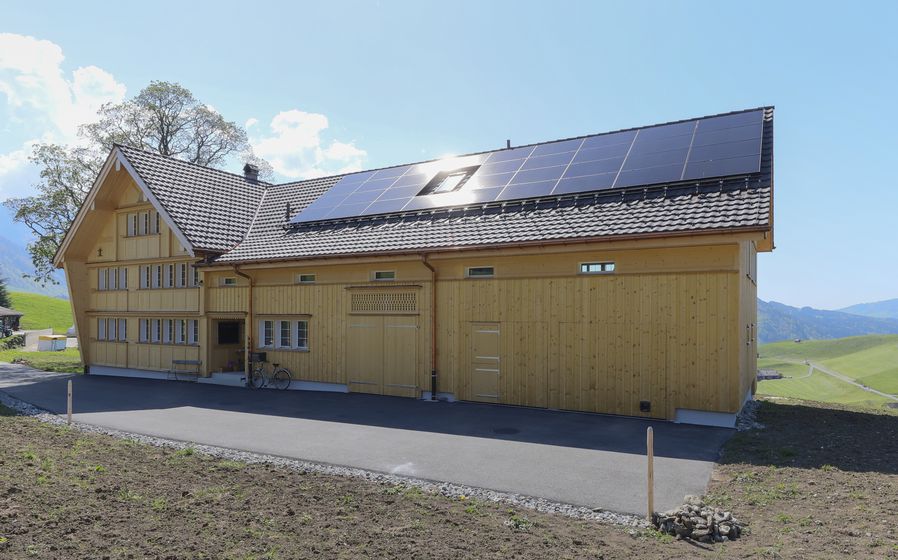 Modernes Holzhaus mit Solarpanelen auf dem Dach in ländlicher Umgebung.