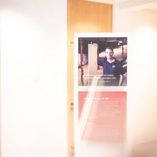 Ein Plakat in einem hell beleuchteten Raum präsentiert einen Mann mit einem Holzbrett, symbolisch für die Dienstleistungen der Stark AG Altstätten im Bereich Holzhandel und Innenausbau.