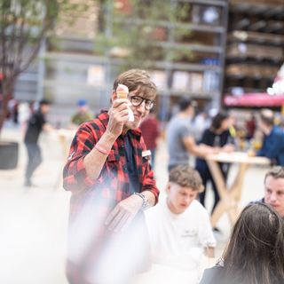 Person in einer Veranstaltungshalle, die ein Eis hält, während Menschen im Hintergrund an Tischen sitzen.