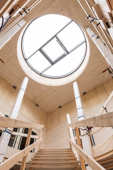 Innenansicht eines modernen Holzgebäudes mit rundem Dachfenster und Holzverkleidung.