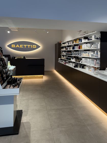 Modern gestalteter Raum mit beleuchtetem Regal und Tresen, Markenname 'Baettig' an der Wand.