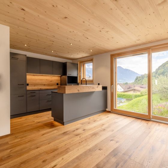 Moderne Küche mit Holzverkleidung, grossen Fenstern und Alpenblick.
