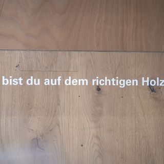 Holzboden mit dem Text 'Hier bist du auf dem richtigen Holzweg'.