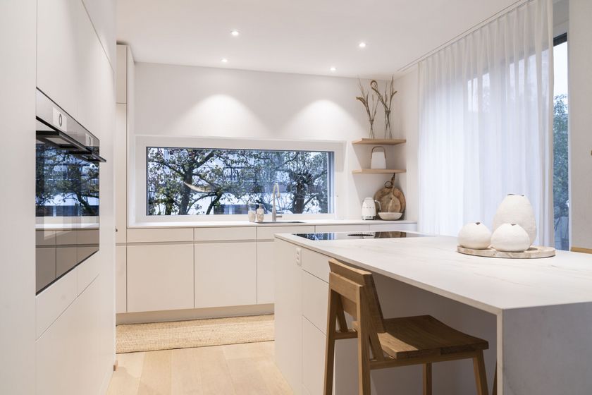 Moderne Küche mit grossem Fenster, stilvollen weißen Schränken und Holzakzenten.