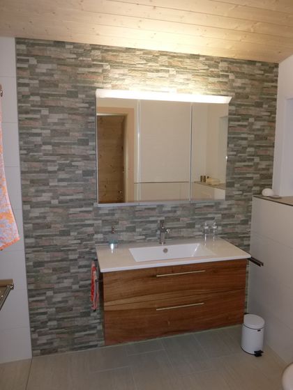 Badezimmer mit Waschbecken, Holzverkleidung und Spiegel auf Steinwand.