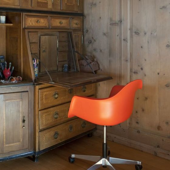 Rustikales Holzinterieur mit rotem Stuhl vor einem antiken Sekretär.