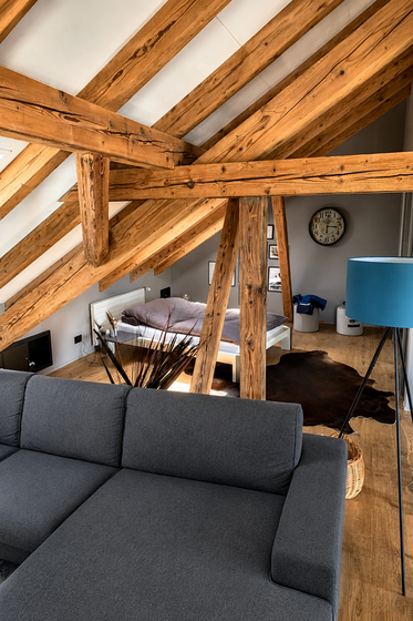 Modernes Dachgeschosszimmer mit Holzbalken und grauer Couch.