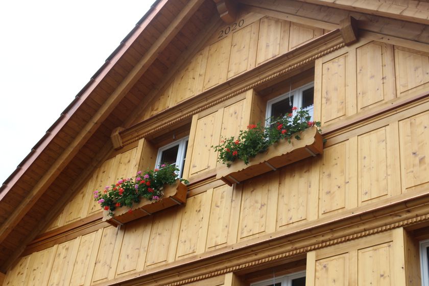 Holzfassade eines traditionellen Hauses mit blühenden Blumenkästen.