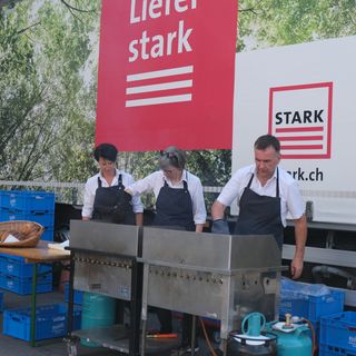 Drei Personen grillen vor einem Stark AG LKW mit Naturmotiv.