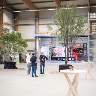 Men talking in a spacious room with plants and a Stark AG branded truck in the background.