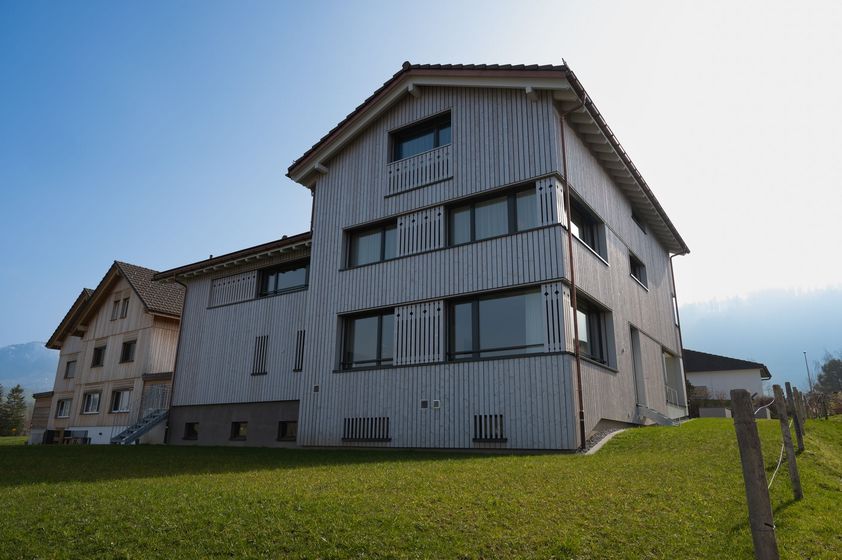 Zweistöckiges Gebäude mit hölzerner Fassade und modernen Fenstern vor klarer Himmelkulisse.
