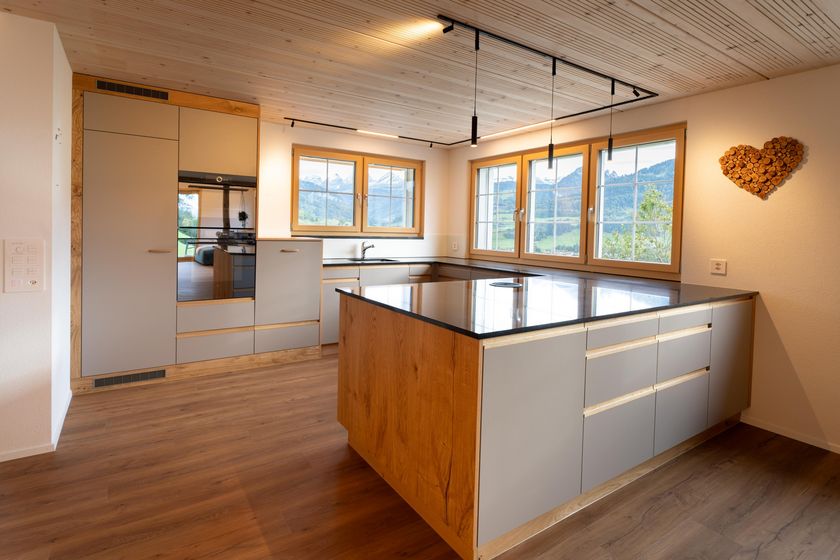 Moderne Küche mit grossen Fenstern und Holzverkleidung.